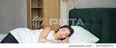 Beautiful asian girl sleeping in her bed, lying in bedroom with closed eyes under white sheets, warm winter duvet Beautiful asian girl sleeping in her bed, lying in bedroom with closed eyes under white sheets, warm winter duvet 107860470