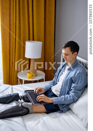guy with artificial legs using laptop for work or studies, having online work at home 107860535