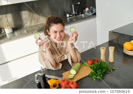 Portrait of beautiful brunette girl chopping vegetables for meal, making salad in the kitchen, eating healthy food, preparing dinner Portrait of beautiful brunette girl chopping vegetables for meal, making salad in the kitchen, eating healthy food, preparing dinner 107860628