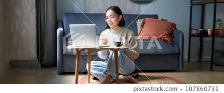 Portrait of beautiful young woman professional, working on remote from home, freelancing with her laptop, video chats, drinks coffee 107860731