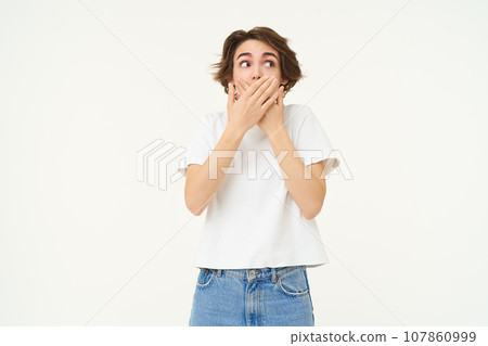 Portrait of woman with shocked, surprised face, covers her mouth with hands and gasps in amazement, stands over white background Portrait of woman with shocked, surprised face, covers her mouth with hands and gasps in amazement, stands over white background 107860999