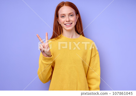 red-haired caucasian woman looking at camera showing victory gesture red-haired caucasian woman looking at camera showing victory gesture 107861045