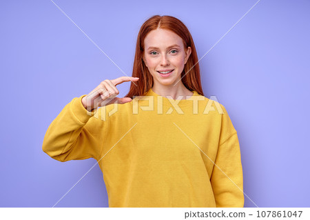 smiling cheerful red-haired girl gesturing with hand doing small size sign 107861047