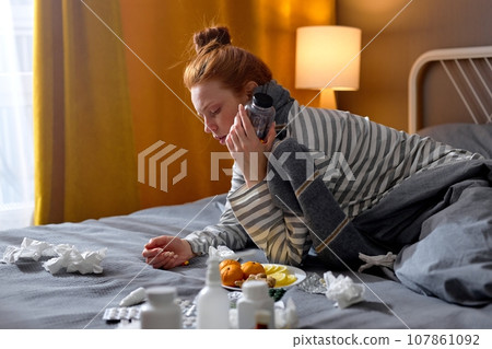 young woman with cold blowing runny nose and swollen throat sitting on bed at home young woman with cold blowing runny nose and swollen throat sitting on bed at home 107861092