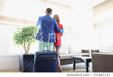 Couple dressed in suits, suitcase behind, enjoy view out of window, wait for flight 107861152