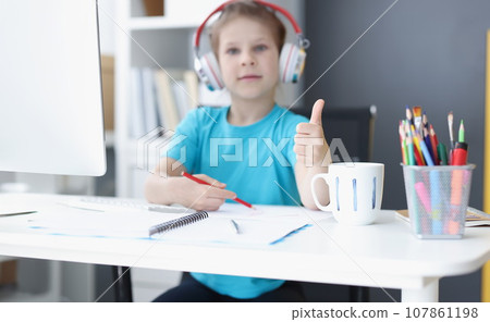 Schoolgirl studying online at home, wear headset, show thumbs up, drawing Schoolgirl studying online at home, wear headset, show thumbs up, drawing 107861198