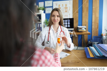 Female doctor give to patient plastic container filled with medication, intern advertises pills 107861219