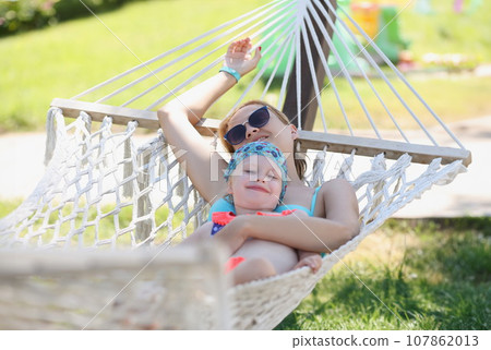 Resting mother embrace daughter, girls lay on hammock in shadow, enjoy life, time with family Resting mother embrace daughter, girls lay on hammock in shadow, enjoy life, time with family 107862013