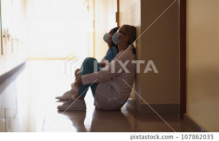 Exhausted nurses after hard long surgery sitting on floor in hall, difficult shift Exhausted nurses after hard long surgery sitting on floor in hall, difficult shift 107862035