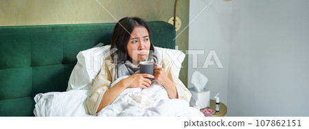 Flu, sickness and people. Young woman feeling sick, having fever and catching col, lying in bed with hot tea, taking drugs from influenza 107862151