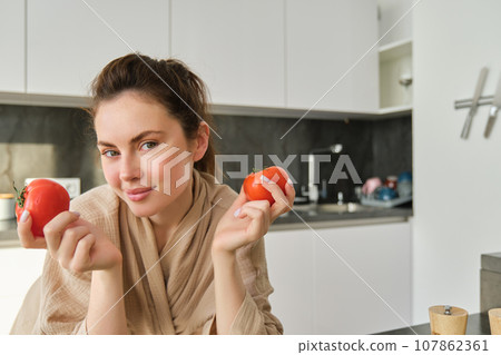Portrait of beautiful woman cooking in the kitchen, chopping vegetables on board, holding tomatoes, lead healthy lifestyle with preparing fresh salads, vegan meals 107862361