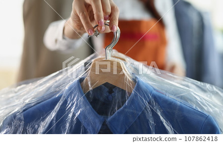 Worker giving to client clean clothes hanging on hangers at dry cleaning company 107862418