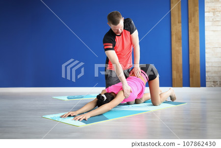 Man partner support woman in stretching on mat, yoga class for health 107862430
