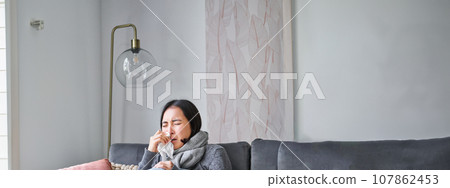 Korean woman feels unwell, sneezing and coughing, catching cold, staying at home with fever and temperature, taking medication Korean woman feels unwell, sneezing and coughing, catching cold, staying at home with fever and temperature, taking medication 107862453