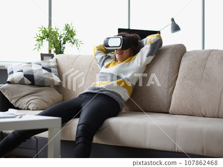Female lay casually on couch in vr glasses, use modern device at home, test new development Female lay casually on couch in vr glasses, use modern device at home, test new development 107862468