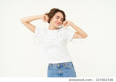 Portrait of smiling, pleased woman stretching hands, waking up after sleep, standing over white background Portrait of smiling, pleased woman stretching hands, waking up after sleep, standing over white background 107862586