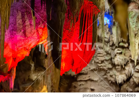Karst cave, amazing view of stalactites and stalagnites in colorful bright light, beautiful natural landmark in touristic place. 107864069