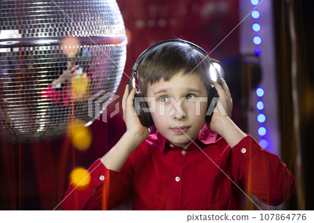 A young boy in headphones listens to music on the background of a disco ball. 107864776