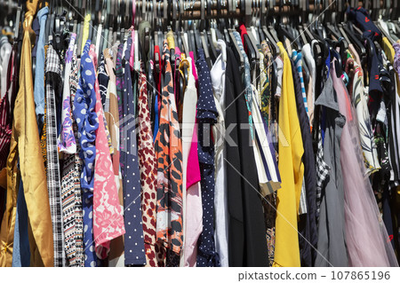 A variety of summer dresses made from budget fabrics hang on hangers. Sale of summer clothes. 107865196