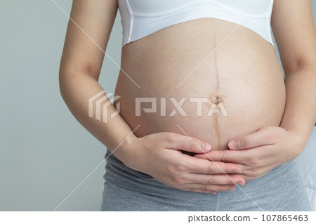 Close up of Young Pregnant Woman holding her hands on her belly in the last trimester of pregnancy. Close up of Young Pregnant Woman holding her hands on her belly in the last trimester of pregnancy. 107865463