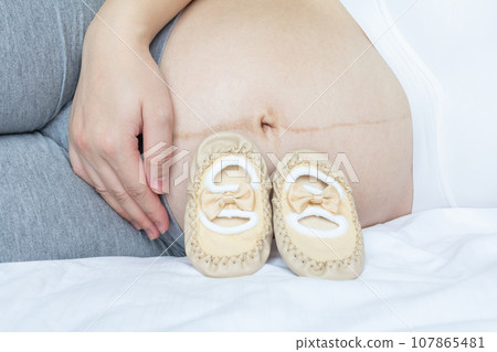 Pregnancy Loving concept. Young pregnant and her baby shoes. Pregnancy Loving concept. Young pregnant and her baby shoes. 107865481