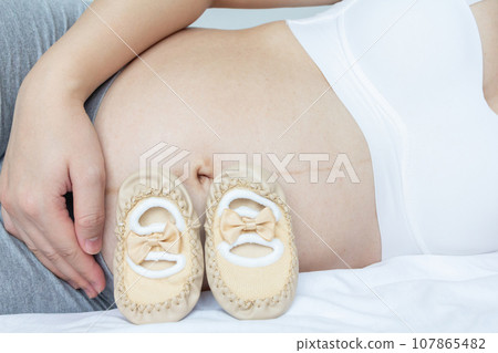 Pregnancy Loving concept. Young pregnant and her baby shoes. Pregnancy Loving concept. Young pregnant and her baby shoes. 107865482
