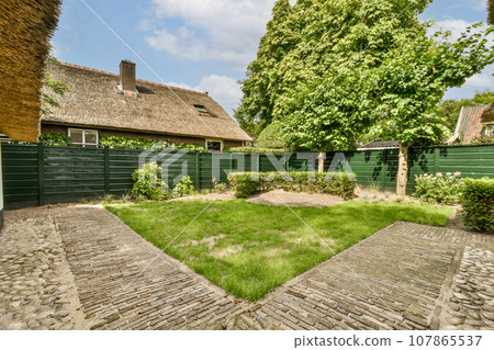 an outside area with grass, trees and brick paversed walkway leading up to a house in the background 107865537
