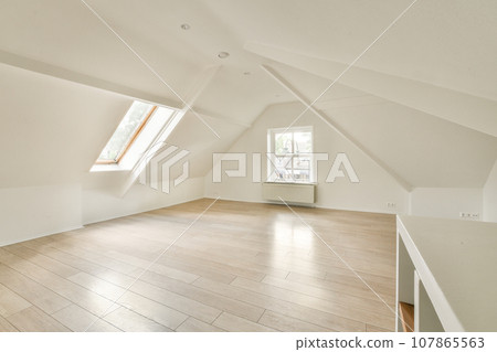 an empty room with wood flooring and white paint on the walls there is a large window in the corner an empty room with wood flooring and white paint on the walls there is a large window in the corner 107865563