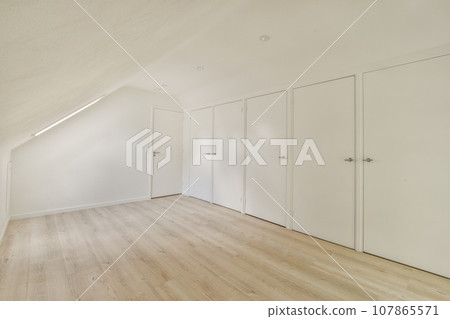 an empty room with white walls and wood flooring on the right side of the room, there are three closed doors an empty room with white walls and wood flooring on the right side of the room, there are three closed doors 107865571