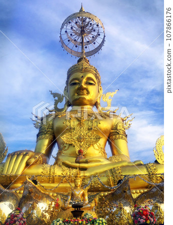 The Big Figurine of Gold Brass Phra Phut Sik Khi Thotsaphon (First Buddha) buddha sculpture statue sit among blue sky to be symbolic of the spiritual. The Big Figurine of Gold Brass Phra Phut Sik Khi Thotsaphon (First Buddha) buddha sculpture statue sit among blue sky to be symbolic of the spiritual. 107866176