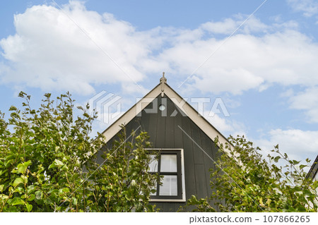 a house with a clock on it's side and some trees in the fore - eye, against a blue sky background 107866265