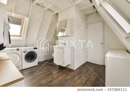 a laundry room with wood flooring and white washer in the space is located on top of an attic loft 107866311