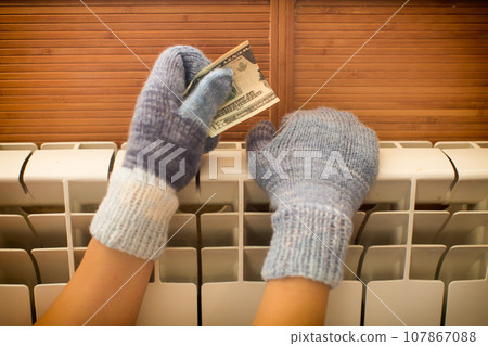 Hands in warm knitted mittens warm themselves on the radiator. 107867088