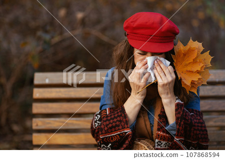 elegant woman blowing nose while sitting on bench in city park 107868594