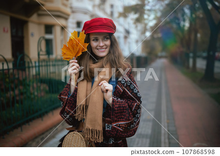 smiling modern woman in red hat with autumn leafs walking 107868598