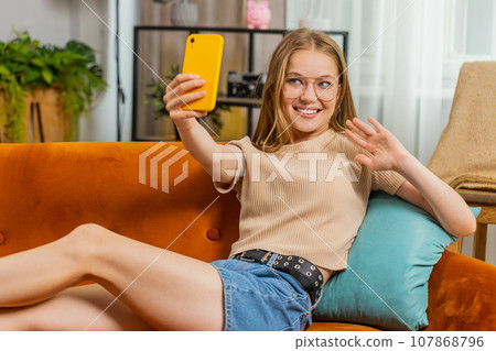 Young blonde woman taking selfie on smartphone communicating video call home online with subscribers Young blonde woman taking selfie on smartphone communicating video call home online with subscribers 107868796