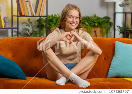 Happy young woman girl makes symbol of love showing heart sign to camera express romantic feelings Happy young woman girl makes symbol of love showing heart sign to camera express romantic feelings 107868797