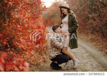 Happy and young pregnant couple in autumn park. People, lifestyle, relaxation and vacations concept. Happy and young pregnant couple in autumn park. People, lifestyle, relaxation and vacations concept. 107869223