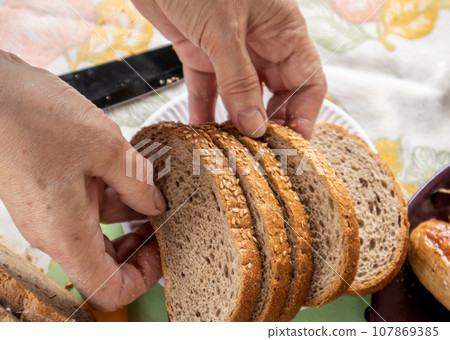 Women's old hands hold slices of whole grain bread with sesame seeds, close-up, selective focus 107869385