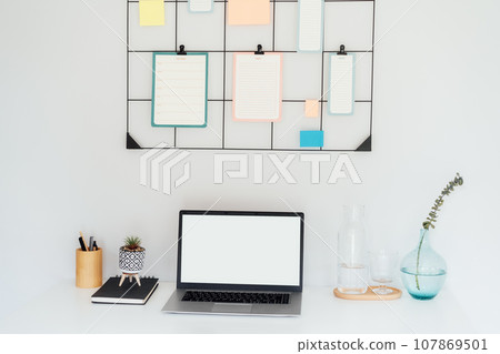 Modern workplace - white desk with laptop mockup empty screen, grid mood board with pinned notes and check lists for plans, office supplies at work space in home office room interior. Modern workplace - white desk with laptop mockup empty screen, grid mood board with pinned notes and check lists for plans, office supplies at work space in home office room interior. 107869501