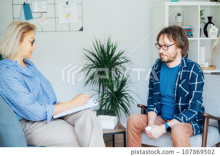 Professional psychotherapy. Female psychologist having session with male patient at mental health clinic, Taking Note During Appointment In Office. Psychological help service. Treatment of depression Professional psychotherapy. Female psychologist having session with male patient at mental health clinic, Taking Note During Appointment In Office. Psychological help service. Treatment of depression 107869502