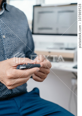 man pricking his finger with a fingerstick in the office 107869528