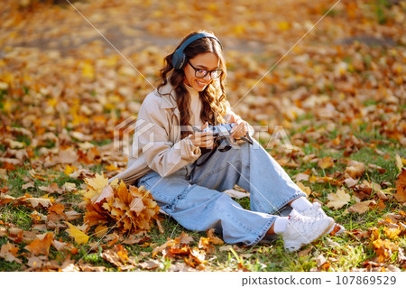 Beautiful woman taking pictures in autumn forest. Woman enjoying autumn weather. Lifestyle concept. 107869529