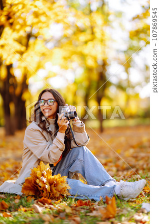 Beautiful woman taking pictures in autumn forest. Woman enjoying autumn weather. Lifestyle concept. 107869545