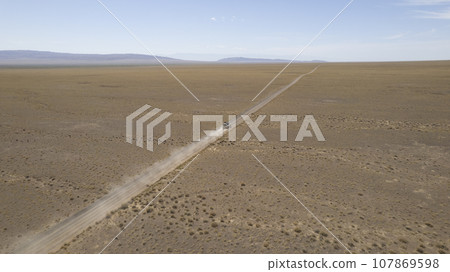 A white SUV is driving fast on a dusty road. Drone 107869598