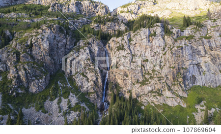 A high waterfall cascades in a mountain gorge A high waterfall cascades in a mountain gorge 107869604