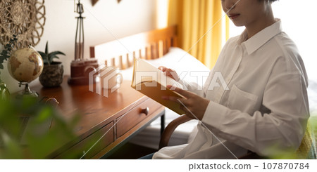 Portrait of a female model with short hair reading in her room at home 107870784