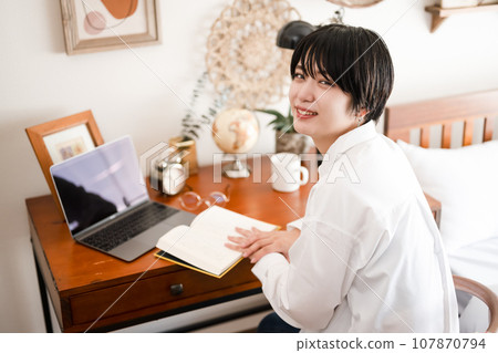Portrait of a female model with short hair reading in her room at home 107870794