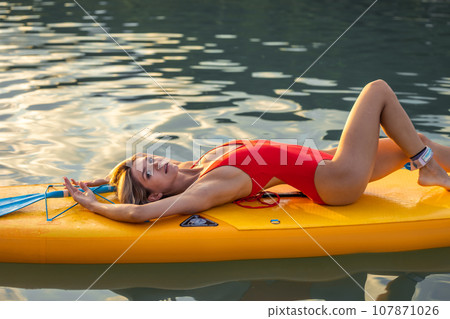 Young woman relaxing in the sea on a SUP board, girl sunbathing on vacation. Young woman relaxing in the sea on a SUP board, girl sunbathing on vacation. 107871026