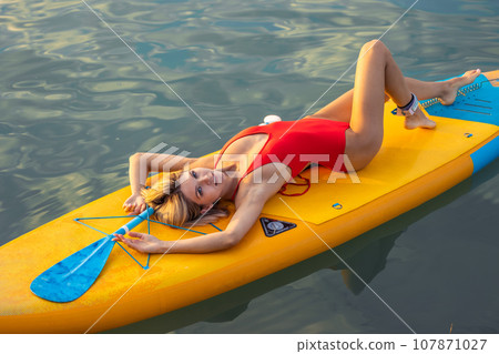 Young woman relaxing in the sea on a SUP board, girl sunbathing on vacation. 107871027